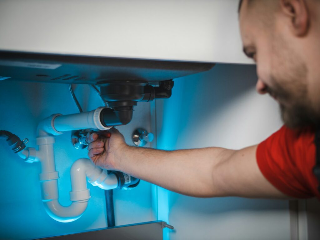 Technician fixing a leaking pipe under a sink